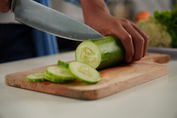 Selective focus on woman's hand chopping cucumber on cutting board