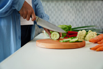 Selective focus on woman's hand chopping cucumber on cutting board