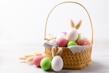 Easter eggs with bunny rabbit ears in basket on white background