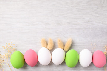 White easter eggs with bunny rabbit ears and colorful easter eggs on white background with copy space, Top view