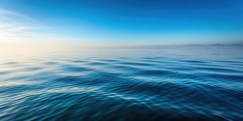 Obraz premium A gentle sea ripple on a calm water surface with morning fog slowly rising from the ocean