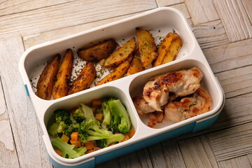 bento set lunch box. potato wedges, chicken steak, and stir-fried broccoli carrots. healthy low-fat...