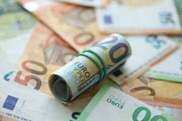 Roll of twenty euro currency bills lies on big amount of hundred and fifty euro banknotes