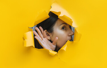 A young girl puts her hand to her ear and listens in surprise, her mouth open through a hole in the...