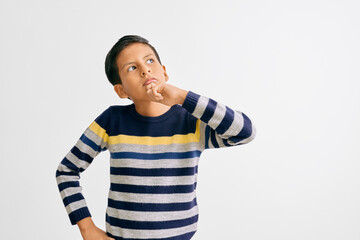 Boy wearing a striped sweater in blue, gray, and yellow, showing a reflective gesture while looking...