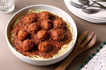 READY TO SERVE FAMILY-STYLE SPAGHETTI AND MEATBALLS  WITH A STACK OF PLATES AND FORKS