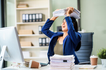 A businesswoman sits at her desk in a modern office, surrounded by numerous documents. She works...