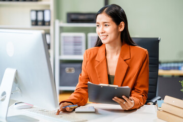 A beautiful Asian businesswoman works at her desk, exuding professionalism and focus.She is deeply...