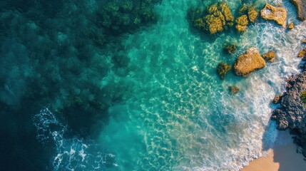 Fototapeta premium Aerial view of turquoise ocean waves crashing on rocky shore and sandy beach.