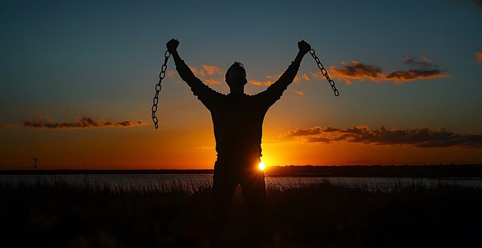 A Protester man breaking chains with a sunrise in the background, symbolizing freedom and dreams coming true. A freedom day concept.