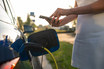 Obraz premium Close up woman hands using a smartphone for payment for charging an electric car 