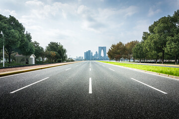 Fototapeta premium Wide Open Road Leading to a Modern City Skyline Surrounded by Lush Trees