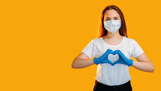 Love signal. Quarantine relationship. Caring woman in protective face mask gloves showing heart gesture isolated on yellow copy space looped. - Powered by Adobe