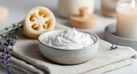 Bowl of white cream surrounded by candles and natural spa items