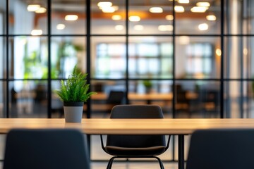 A blurred open-plan office with glass walls, wooden tables, and chairs, soft focus, bokeh effect, and space for text or a logo. A small green plant sits on a table, bathed in warm light