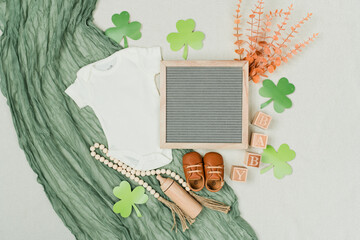 St. Patrick’s Day Baby Flat Lay with White Bodysuit, Shamrock Decor, Wooden Toys and Green...