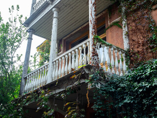 White wooden balcony on second floor with nobody, on an old abandoned house with green ivy densely...