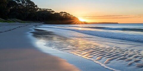 Fototapeta premium Sunrise over tranquil beach with gentle waves and golden light on horizon reflecting on sand.