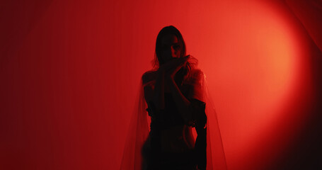 Dance therapy. Calming practice. Peaceful woman silhouette in cellophane rags performing hypnotic hand movements isolated on dark red glowing copy space background.