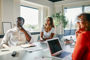 Diverse Team Collaborating in Bright Modern Office Meeting Room. The table is filled with documents, notebooks, and a laptop.