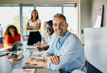 Diverse Team Collaborating in a Bright Modern Office Environment. They all look directly into the camera while smiling. At the end of the table stands the boss with her arms crossed
