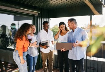Diverse Team Wearing Casual Business Attire, Enjoying Outdoor Meeting and Collaborating on Laptop. They are talking together and looking down at the laptop smiling