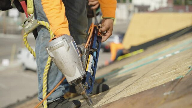 Worker using a nail gun to secure new plywood boards on a residential rooftop during renovation.