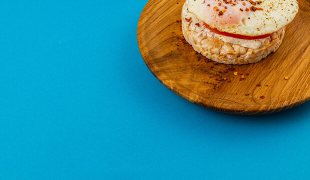 Egg on rice bread with tomato and cheese on a wooden plate on a blue background