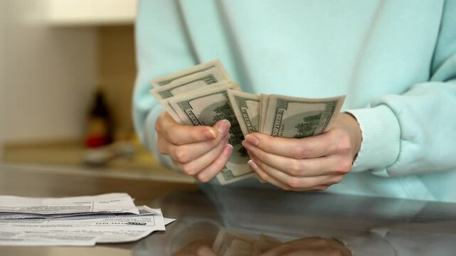 Individual counts cash while surrounded by various bills in a well-lit kitchen. The activity highlights money management and organization at home during a busy day.
