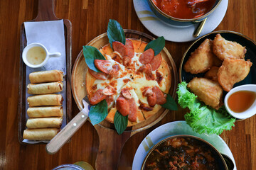 High angle view. The dining table consists of pizza, fried spring rolls, fried fish.