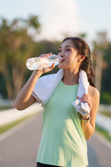 Young asian woman in sportswear enjoying refreshing water from a plastic bottle after an intense...