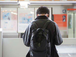冬の朝の駅のホームで電車待ちの若い男性の姿