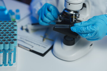 Close-up of scientist's hands in blue gloves placing a glass slide onto a microscope stage,...