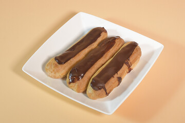 Three eclairs on a white plate on a peach background