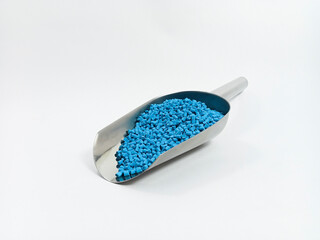 blue masterbatch, polymer carries pigment in stainless steel spoon poured into white background media, suitable for industrial plastic company profile product catalog design