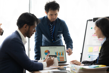 Strategic Business Meeting: Focused team analyzing data on laptop, charts, and whiteboard. ...
