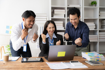 Team Success: Three diverse professionals celebrate their success, hands raised in triumph, in front of a laptop.  The vibrant energy and shared joy capture the essence of teamwork and accomplishment.