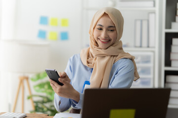 Smiling Muslim businesswoman using calculator and laptop