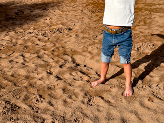 Barefoot caucasian child in jeans playing on sandy beach