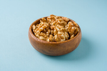 Top view of heap of walnut kernels in wooden bowl on blue background
