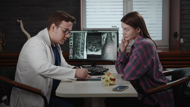 An experienced doctor, osteopath, conducts consultations in a modern clinic. A man consults a patient. The MRI image is open on the computer screen.