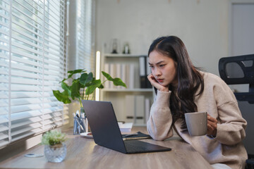 Young asian businesswoman working from home office and having problems, looking worried at laptop...