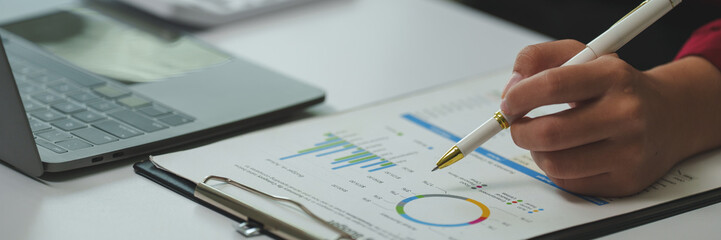 Businesswoman using pen pointing financial chart and graph document on clipboard analyzing...