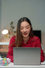 Asian businesswoman working late into the night, focused on her laptop in a cozy home office, balancing remote work and personal ambitions with determination and elegance