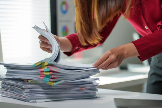 Businesswoman browsing through various documents, efficiently organizing files and managing paperwork in a bustling office environment, tackling deadlines and ensuring smooth operations