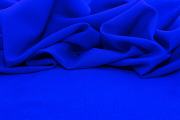 Texture of a smooth luxurious, elegant fabric in blue. Blue satin or silk fabric with folds and...