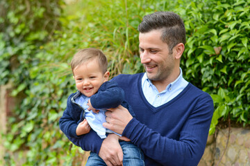 Loving father embracing giggling infant outdoors, radiating joy with gentle smile and affectionate...