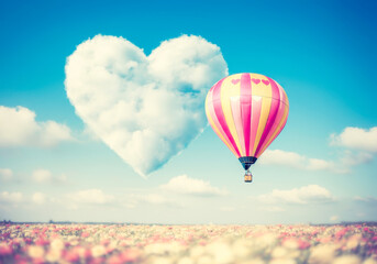 Obraz premium Romantic hot air balloon and heart-shaped cloud above colorful flower field