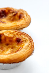 Close up of two freshly baked egg tarts with crispy, flakey pastry isolated on white.