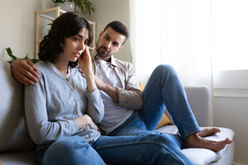 Man consoling sad wife sitting on the sofa at home living room. Copy space.